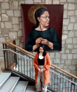 Artist Yehimi Cambrón stands in front of her painting "Estela Tejiendo" in the Turner Lynch Campus Center on Oglethorpe University's campus