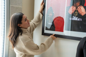 A student carefully hangs art on the wall.